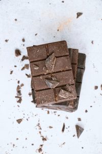 Two milk chocolate bars overlapping each other, some bits are broken off and scattered to portray a strong appetizing look.